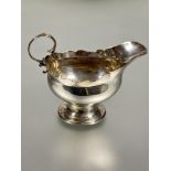 A Edwardian Chester silver milk jug of oval form with scalloped with C scroll handle raised on