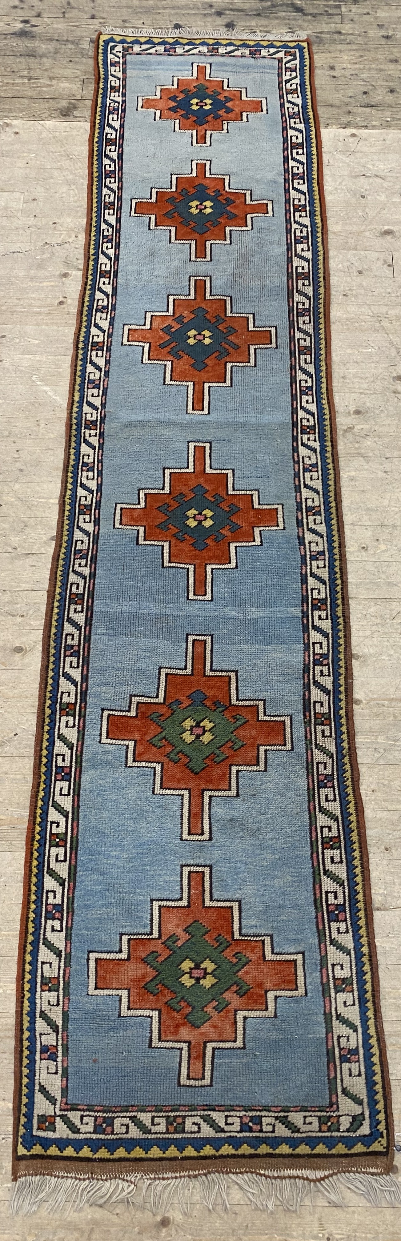 A hand knotted Turkish runner rug, the pale blue field decorated with six geometric medallions,