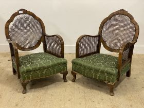 A pair of 1930's walnut framed bergere chairs, each with cane panelled back and sides, raised on