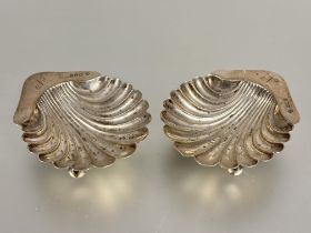 A pair of Edwardian London silver shell shaped butter dishes engraved with initial N raised on three