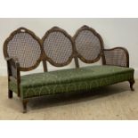 A 1930's walnut framed bergere three seat sofa, with cane panelled back and sides, raised on
