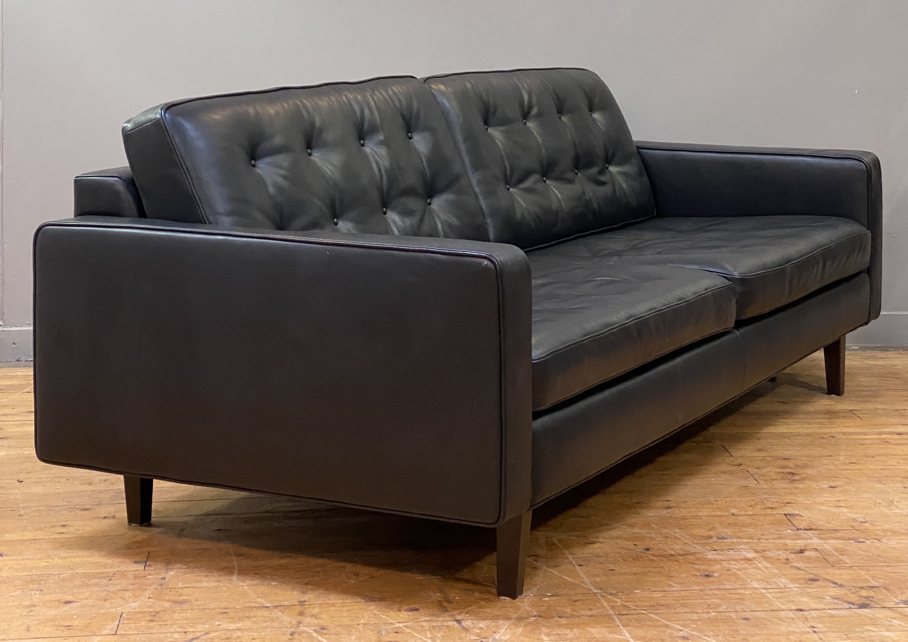 Heals, a contemporary sofa, upholstered in buttoned semi-aniline black leather and standing on