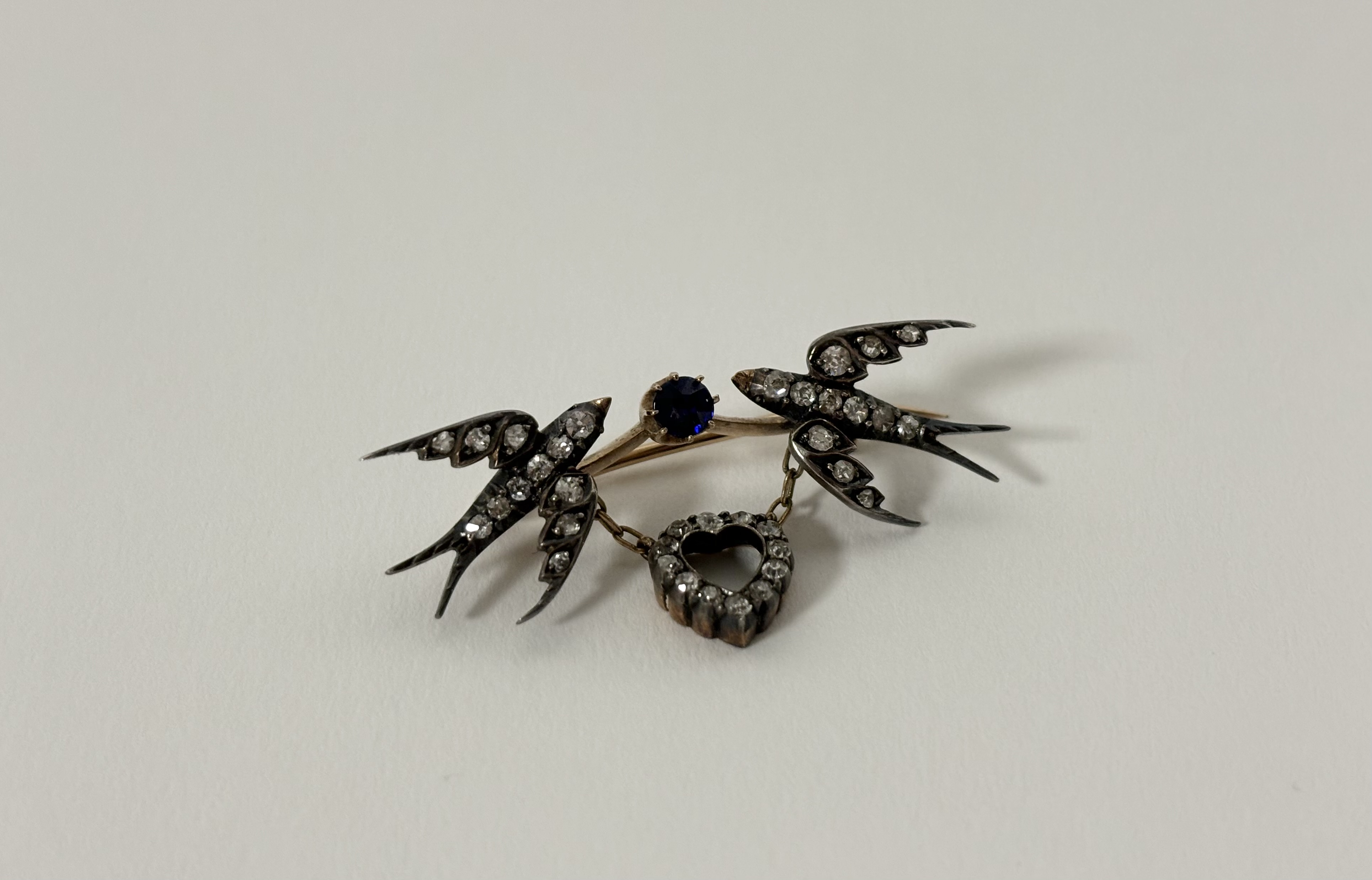 A late Victorian diamond and sapphire brooch modelled as a pair of swallows suspending a heart,
