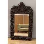 A Black Forest oak wall-hanging mirror, late 19th century, the frame profusely carved with masks and