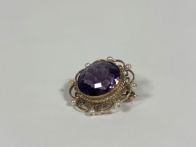 A 9ct gold amethyst brooch, the round-cut stone collet-set in a scroll-cast frame set with seed