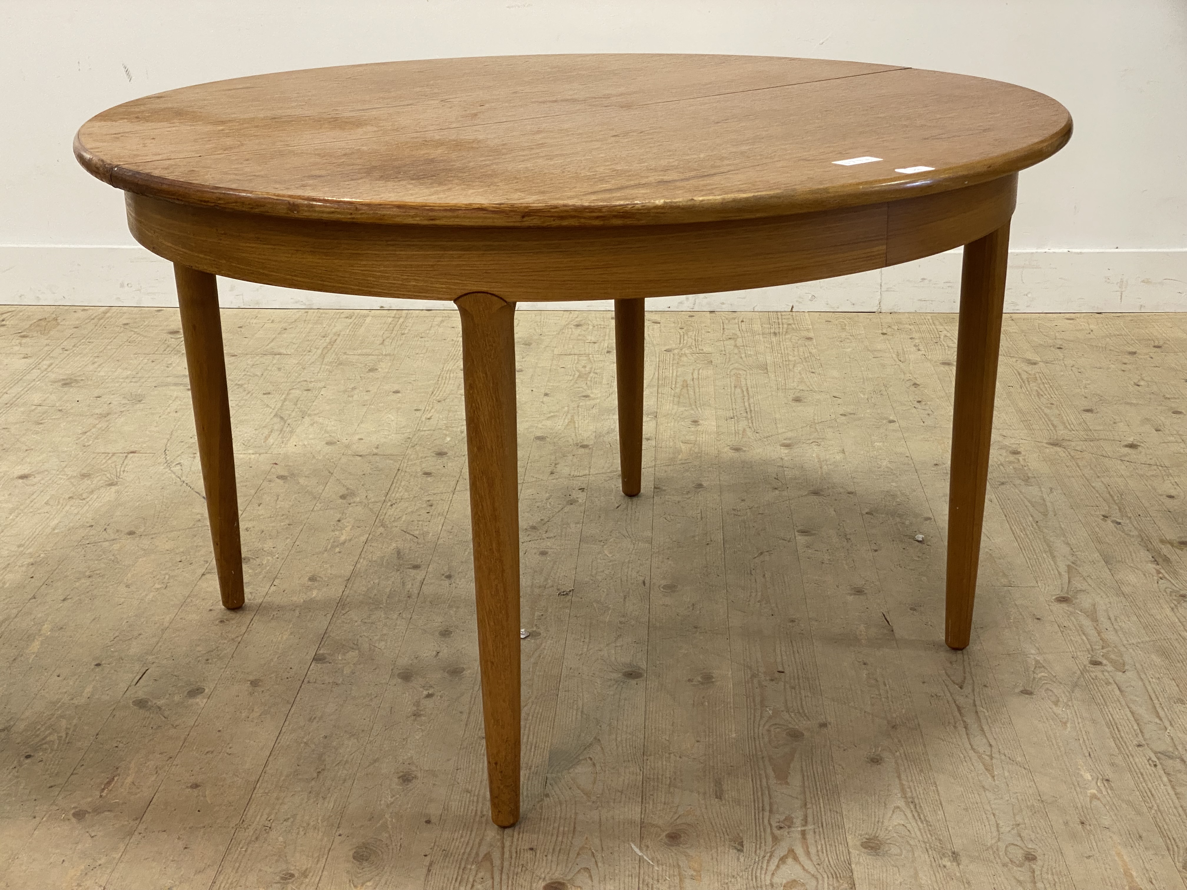A mid century teak circular dining table with magic leaf to centre and raised on turned and