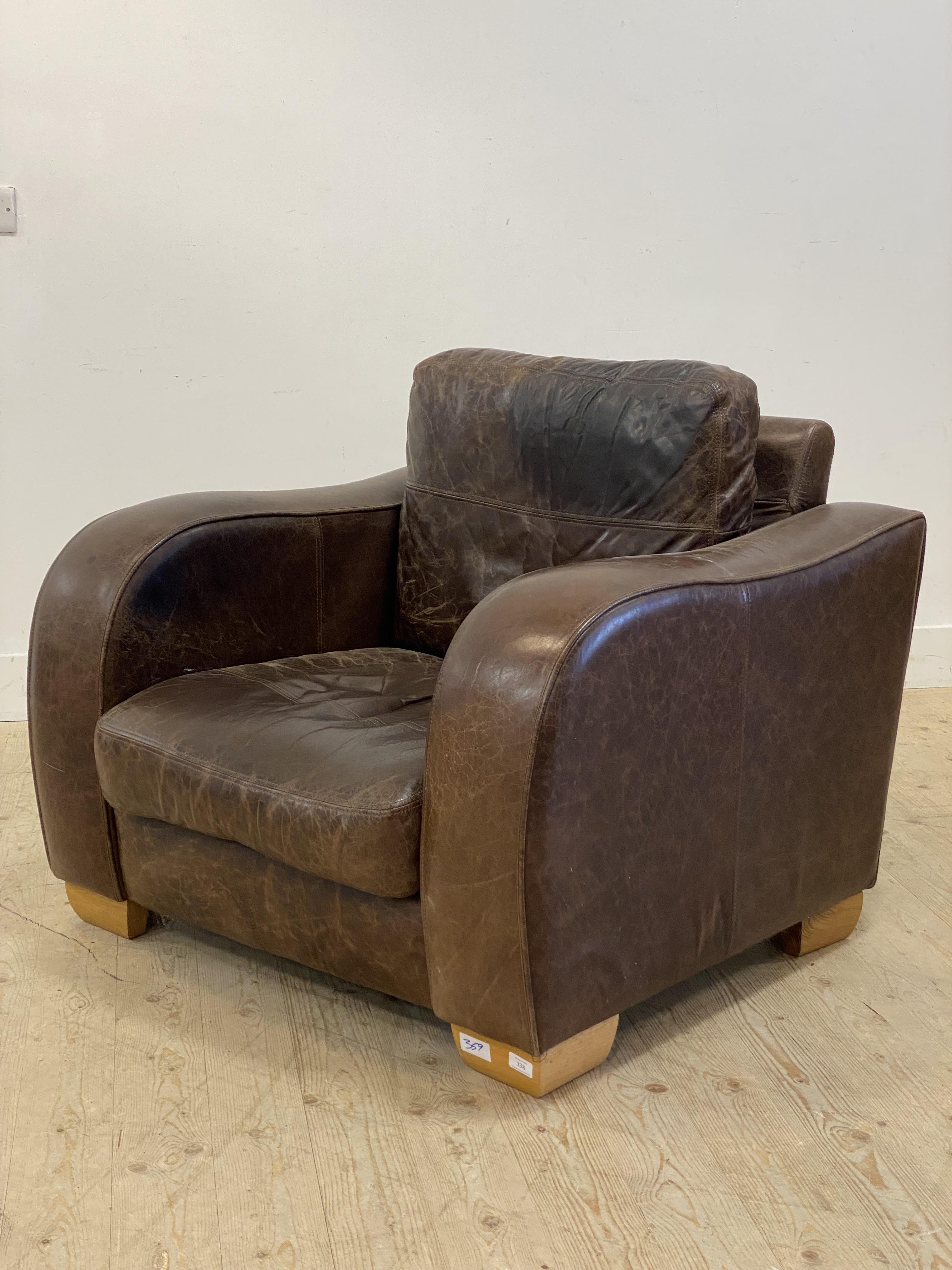 A contemporary brown leather upholstered armchair, raised on block supports. H87cm, 97cm x 97cm.