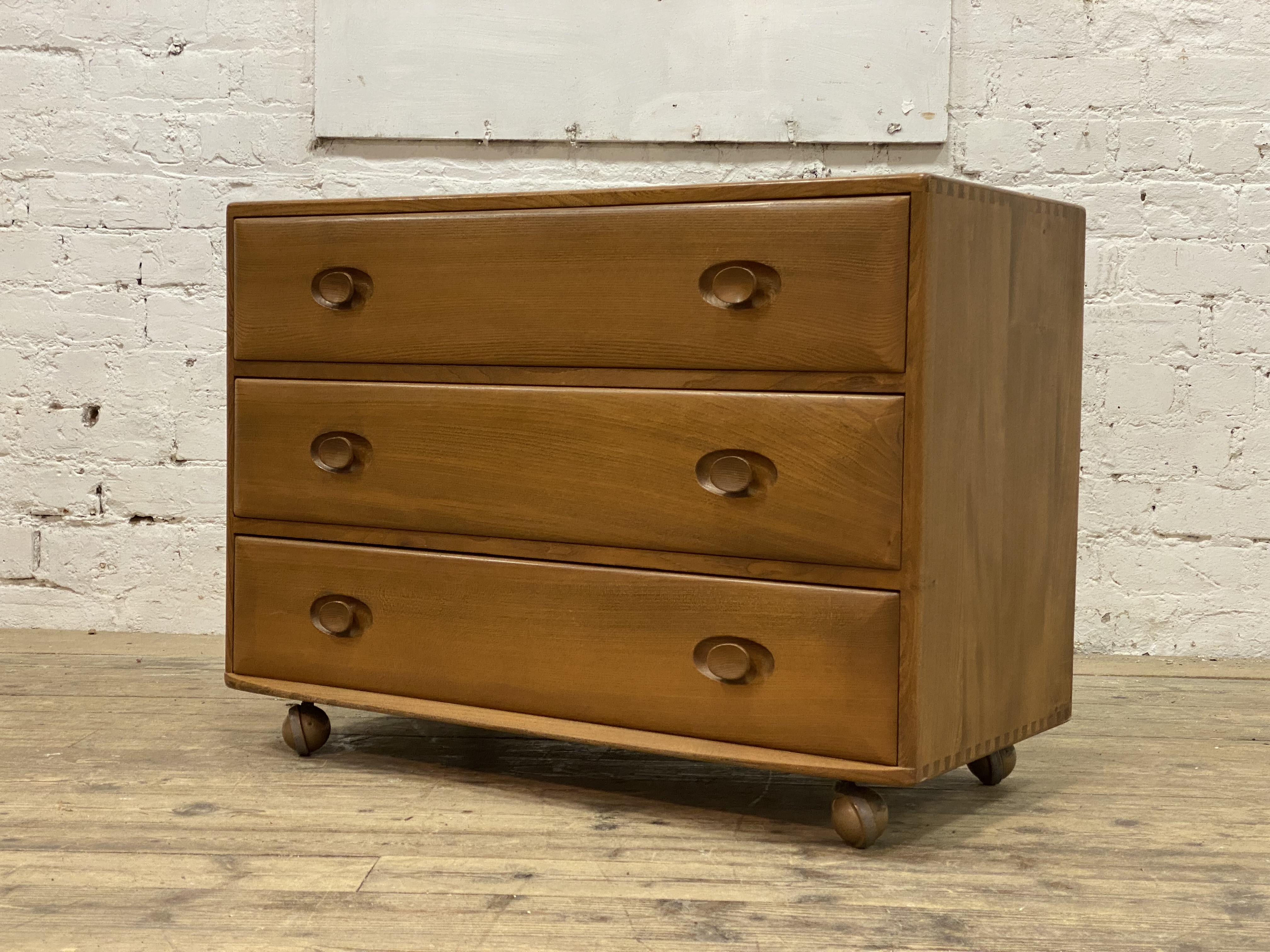 Ercol, a beech chest fitted with three drawers, and moving on castors. H67cm, W92cm, D45cm.