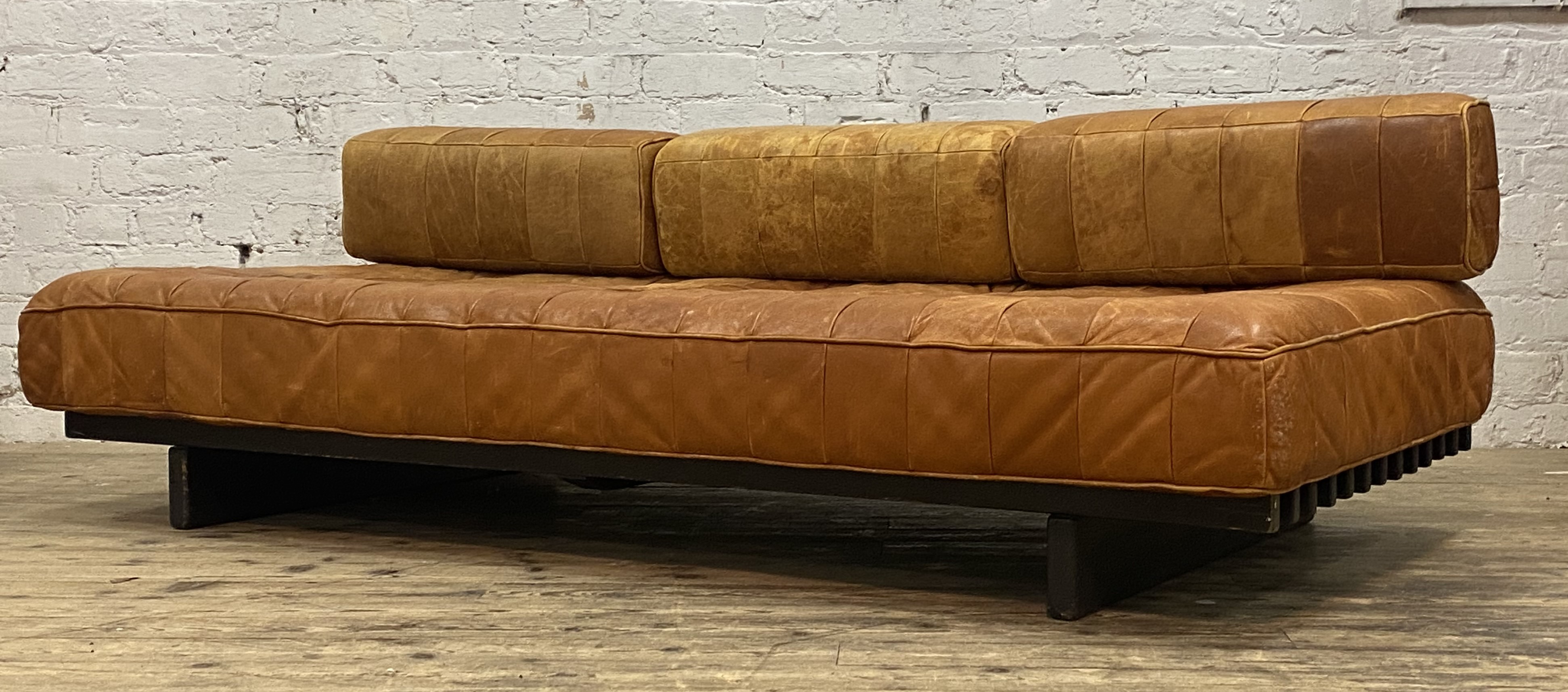 Heals, a mid century low sofa, circa 1980, the squab cushions upholstered in tan leather, and raised