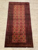 A hand knotted Afghani rug, the red field with repeating lozenges, the deep border with running