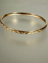 A 9ct gold stiff sprung bangle with half engraved diamond design and clip fastening to side no signs