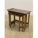 A mid 20th century walnut nest of three tables, each with a rectangular tray top raised on square