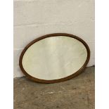 An Edwardian mahogany framed oval wall hanging mirror with bevelled glass. 77cm x 51cm.