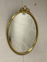 A traditional oval gilt framed wall hanging mirror with bow ribbon surmount. 58cm x 41cm.