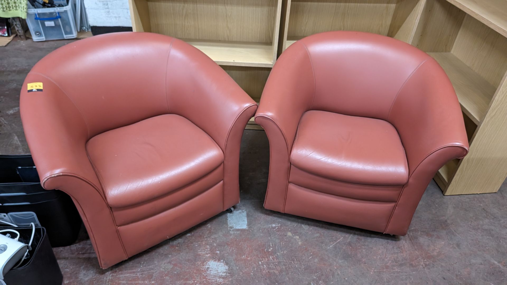 Pair of tub chairs on wheels in dark salmon/terracotta leather/pleather finish