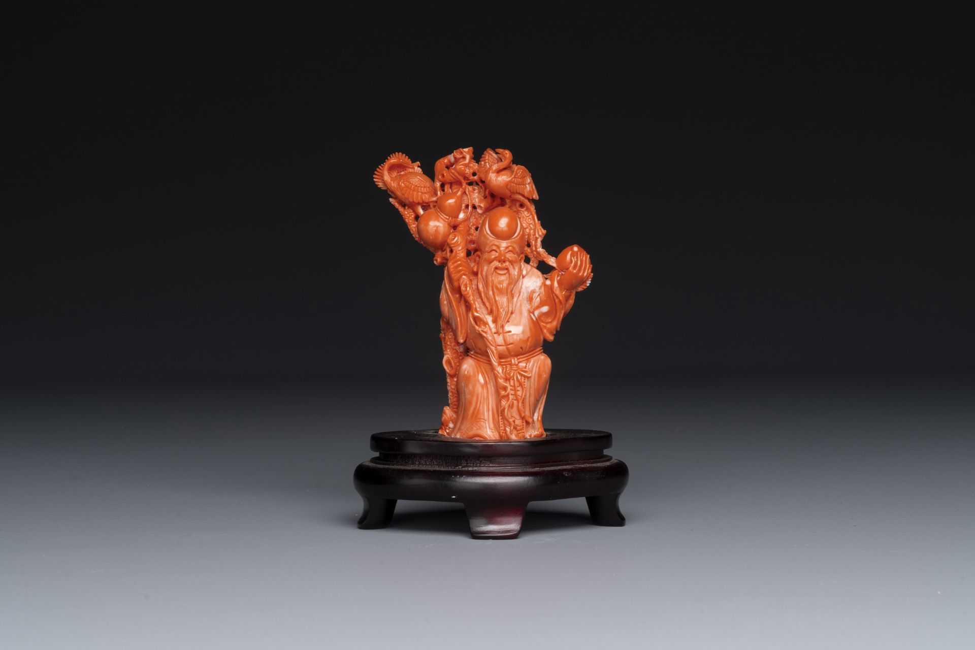 A Chinese red coral figure of Shoulao on wooden stand, 19/20th C.