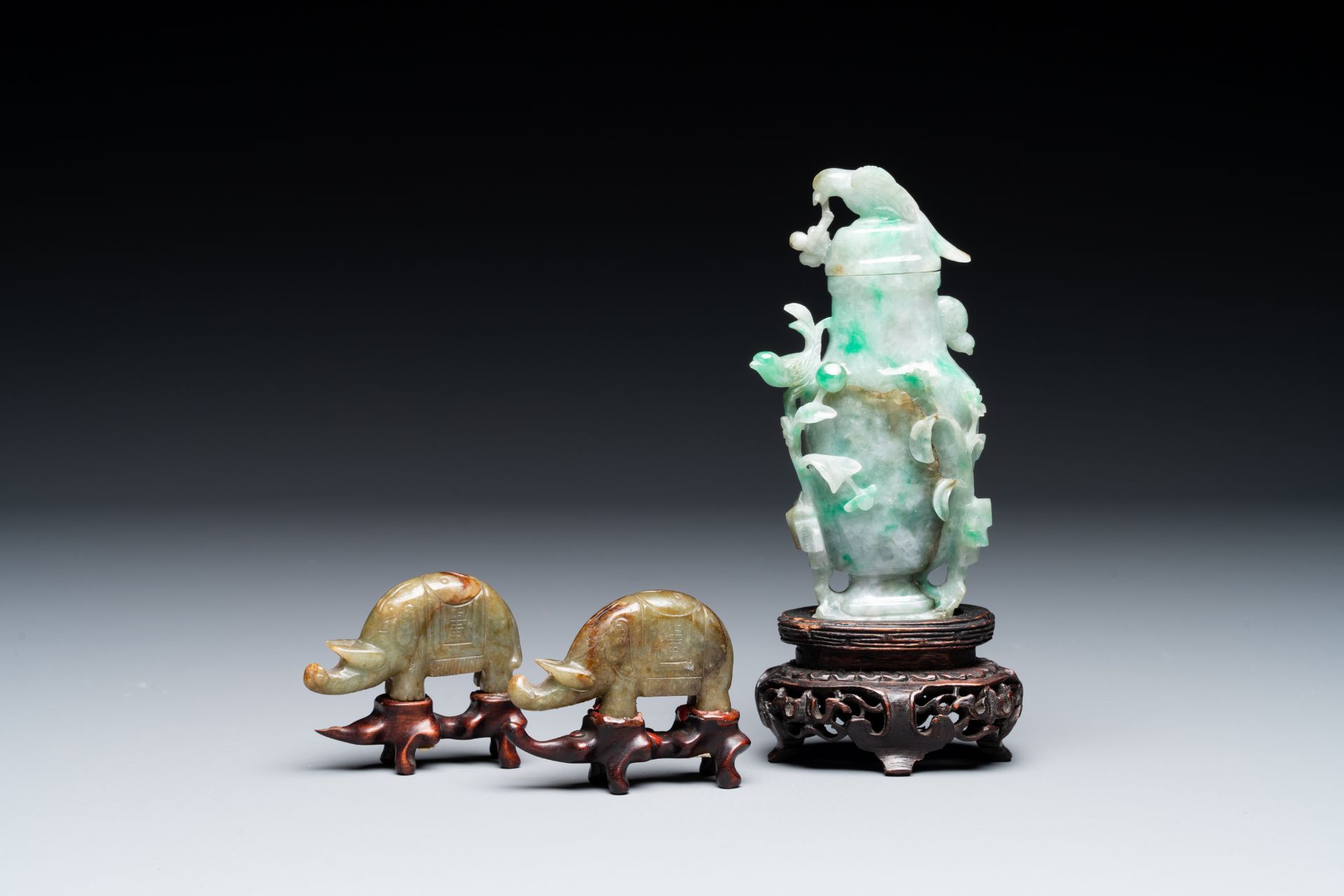 A pair of Chinese jade sculptures of elephants and a lidded vase on wooden stands, 19th C.