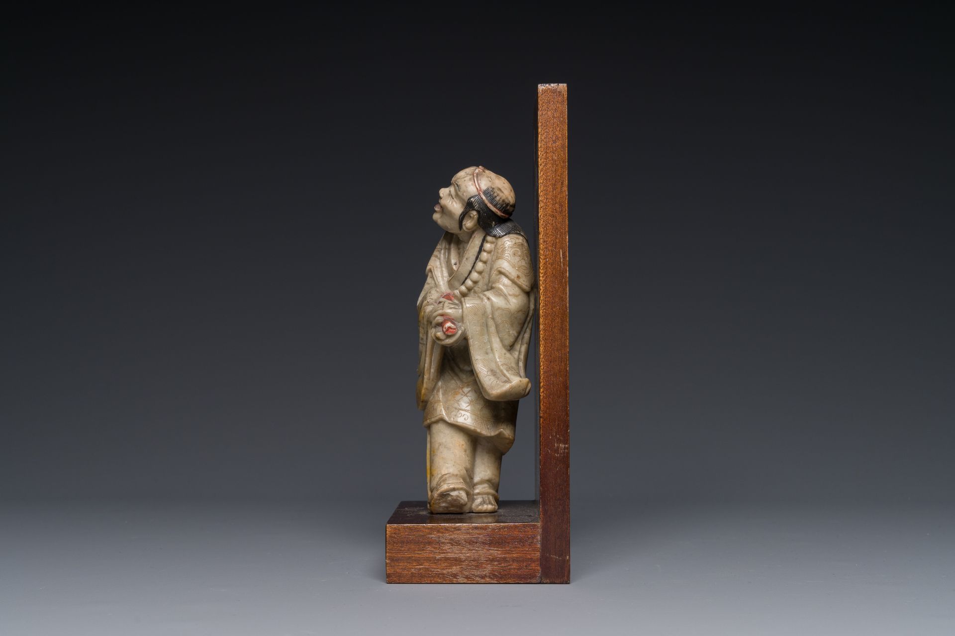 A Chinese partly polychromed soapstone figure on a wooden base, 18th C. - Image 2 of 4