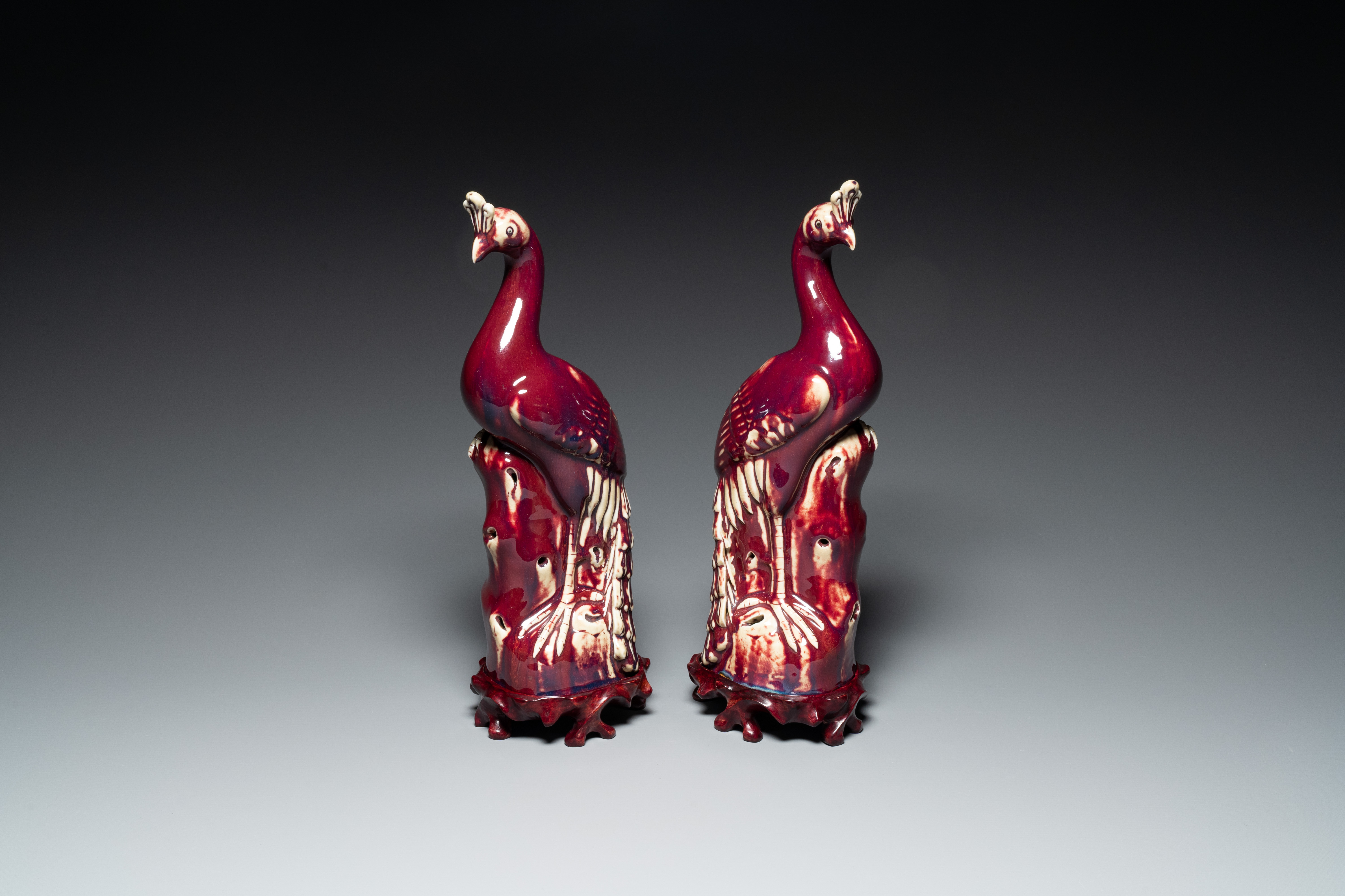 A pair of Chinese flambe-glazed models of peacocks on wooden stands, 19th C.