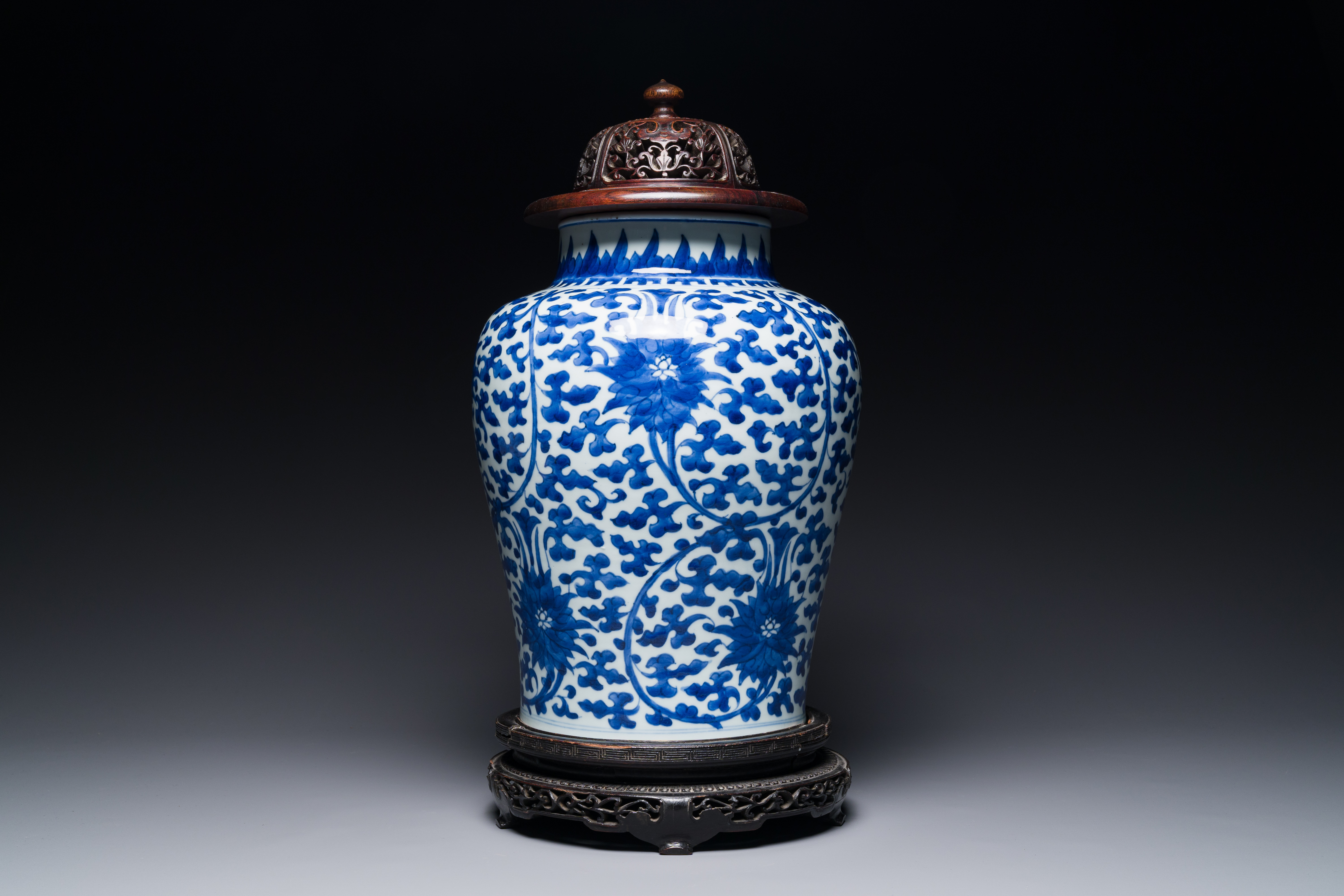 A Chinese blue and white 'lotus scroll' jar with wooden cover and stand, Kangxi