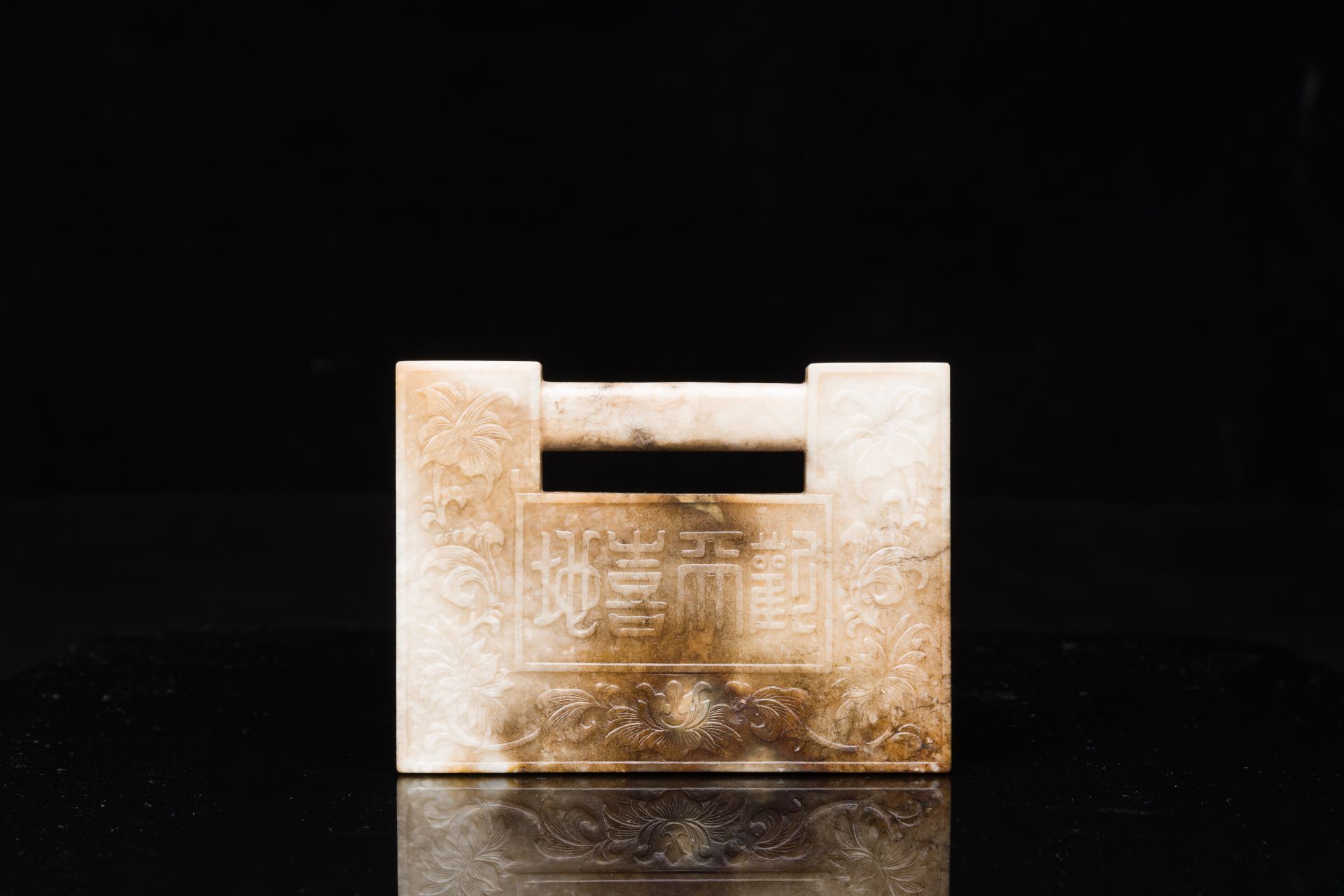 A Chinese white and russet jade lock-shaped plaque with inscription 'Huan Tian Xi Di æ­¡å¤©å–œåœ°',