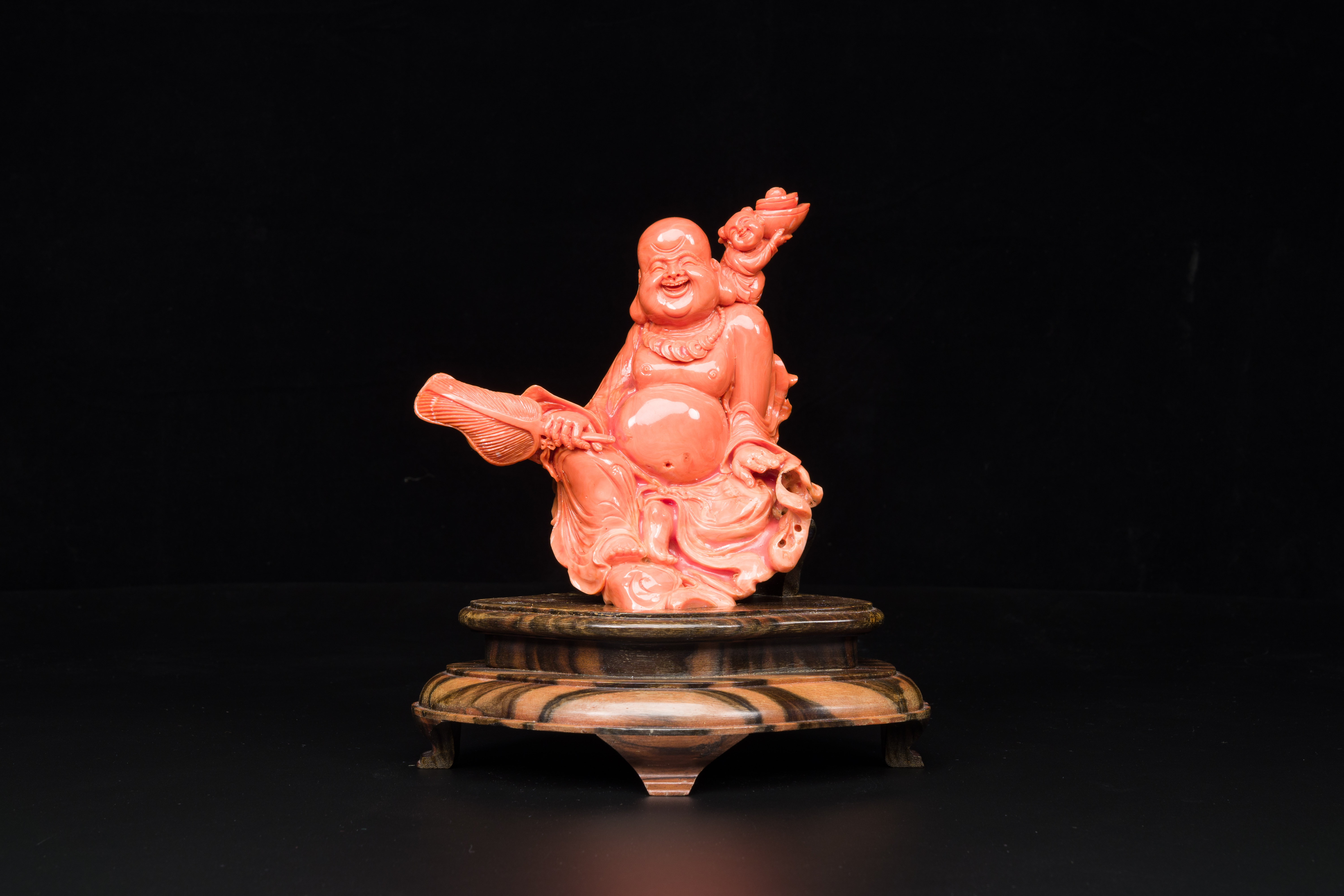 A Chinese red coral figure of a laughing Buddha on wooden stand, 19/20th C.