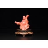 A Chinese red coral figure of a laughing Buddha on wooden stand, 19/20th C.