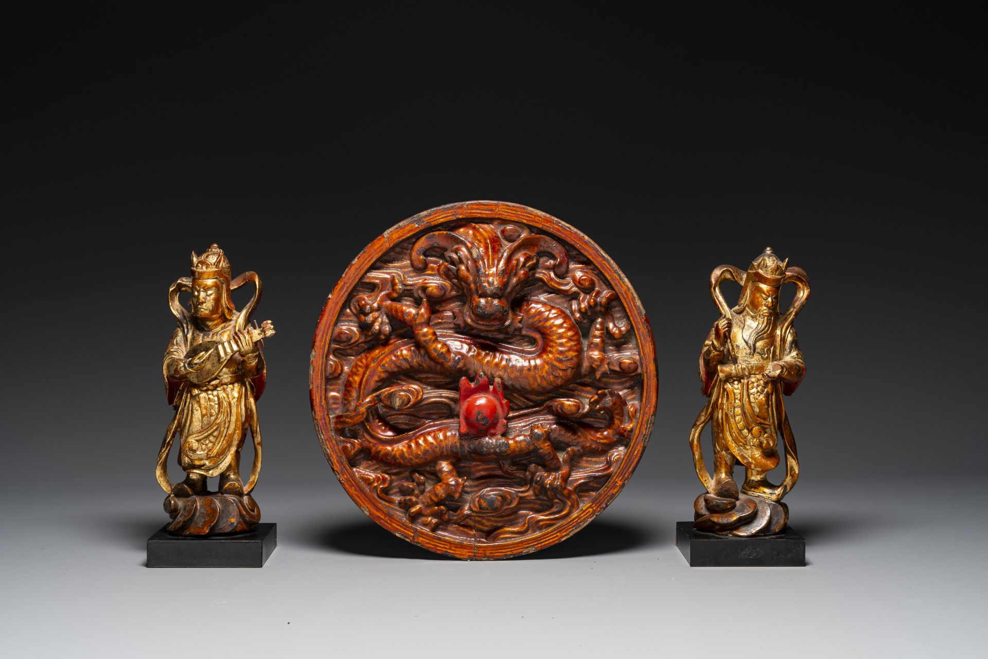 A pair of Chinese gilt-lacquered wooden guardians and a round 'dragon' plaque, 19th C.