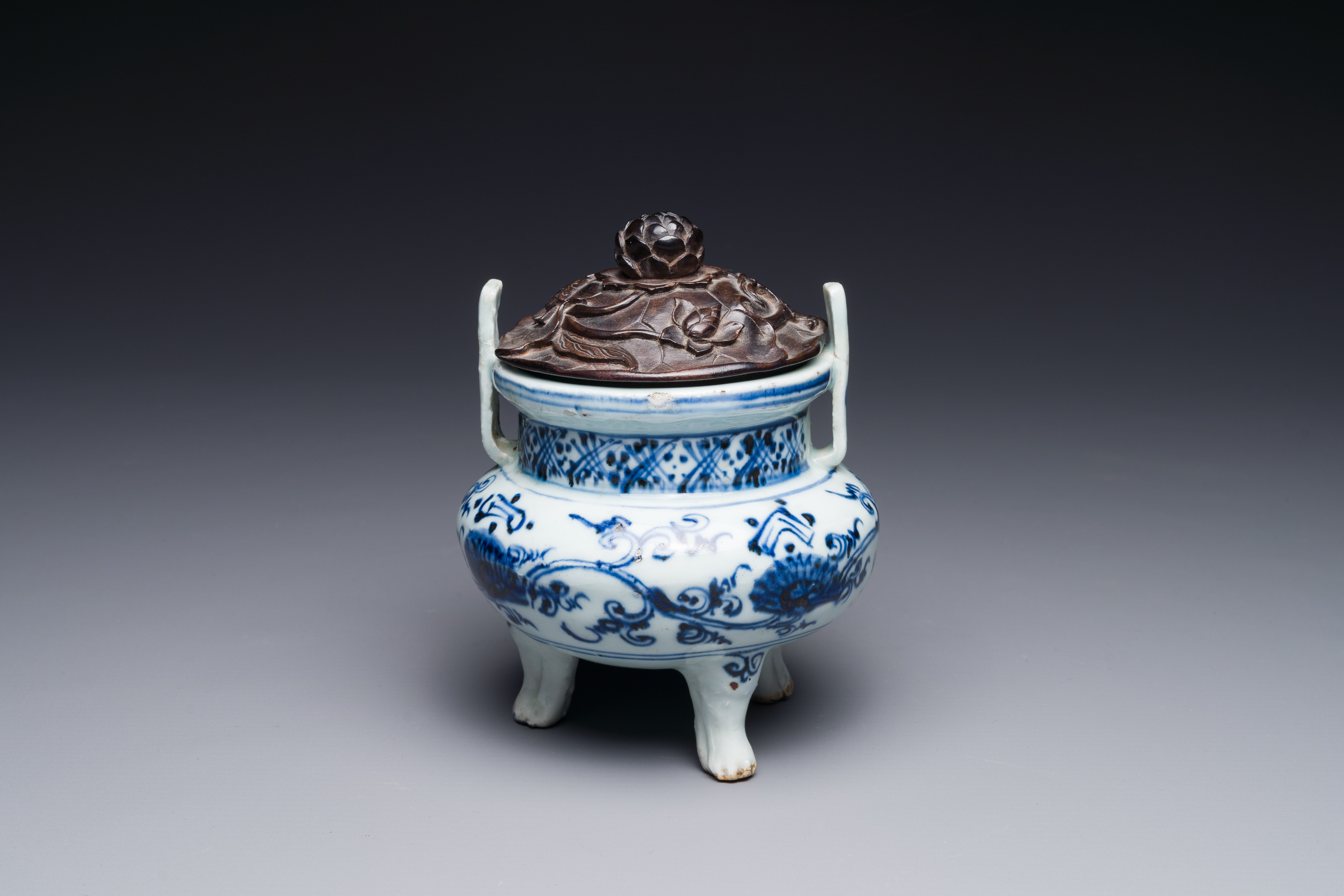 A Chinese blue and white tripod censer with floral design and a wooden cover, Ming