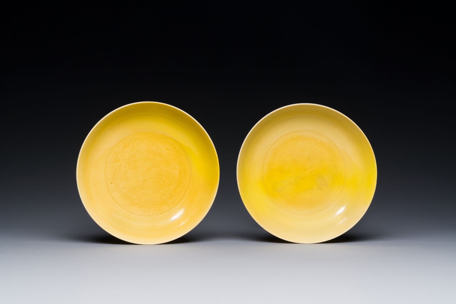 A pair of Chinese monochrome yellow-glazed saucers with incised designs of pine and cranes, Yongzhen