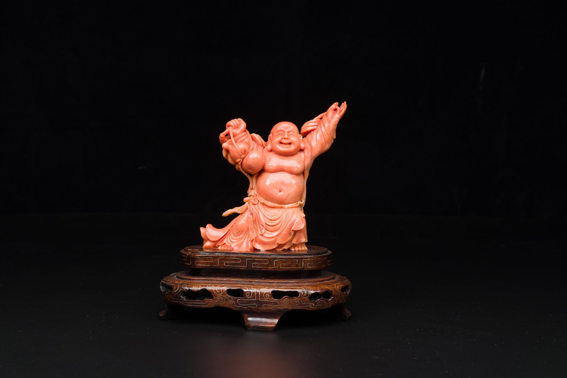 A Chinese red coral figure of a laughing Buddha on wooden stand, 19/20th C.