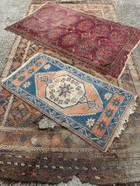THREE EASTERN STYLE WOOLEN RUGS IN WORN CONDITIONS, comprising a larger rust ground example,