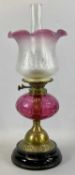 VICTORIAN OIL LAMP, with black ceramic base, embossed brass column, facetted circular cranberry