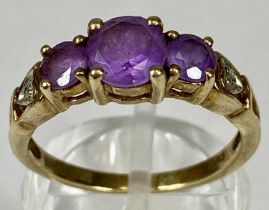 9CT GOLD RING, set with a band of three graduated amethysts, with diamond chips to the shoulders,