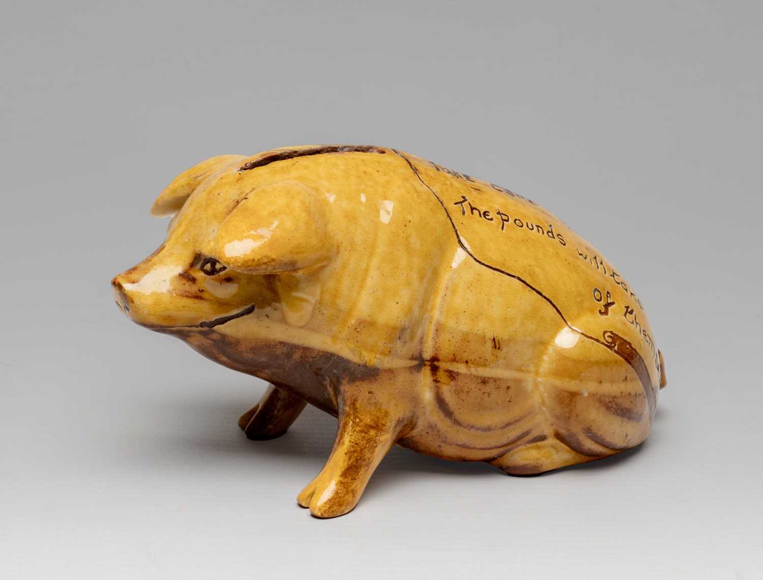 EWENNY SLIPWARE POTTERY MODEL OF A SEATED PIG with coin slot at the top, yellow and brown glaze