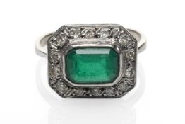 WHITE METAL EMERALD & DIAMOND CHIP CLUSTER RING, the central emerald (8 x 6mms) within a border of