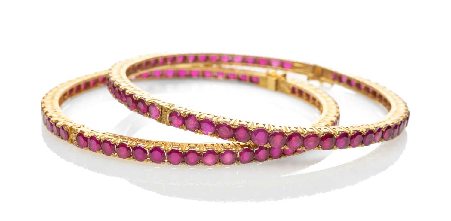 TWO SIMILAR YELLOW METAL BELIEVED RUBY SET HINGED BANGLES, one stamped '22K' the other stamped '