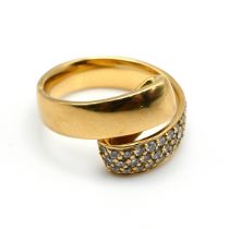 A diamond set cross over dress ring, stamped ‘750’, one half pave set with thirty eight small bri...