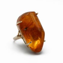 An gold amber ring, the large asymmetrical stone having a bug inclusion, the shank unmarked, in a...