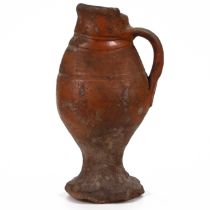 A small naive earthenware jug with pie crust foot. Dates c15th-17th Century. An old label to the ...