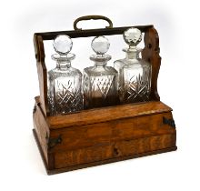 An Edwardian oak tantalus with locking bar containing three square form decanters. The brass boun...