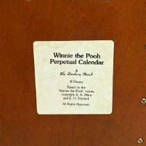 A Danbury Mint Winnie The Pooh perpetual calendar, on a wooden display cabinet