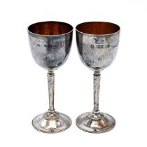 A pair of Elizabeth II silver hammered goblets, on tapering stem and standing on a circular base,...