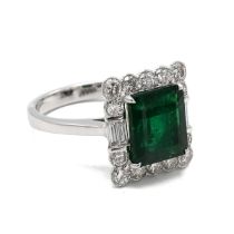 An 18k white gold emerald and diamond square cluster ring, set with an octagonal step cut emerald...