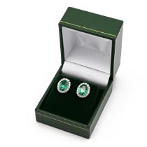 A pair of 18k white gold emerald and diamond oval cluster earrings, set with oval mixed cut emera...