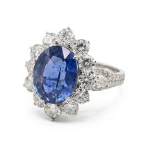 An 18k white gold sapphire and diamond oval cluster ring, set with an oval mixed cut sapphire 7.0...
