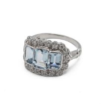 An 18k white gold aquamarine and diamond dress ring, set with three emerald cut aquamarines, with...