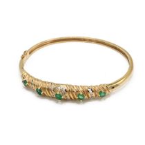 A 14ct gold, diamond and emerald set bangle, set with five oval cut emeralds and twenty four bril...