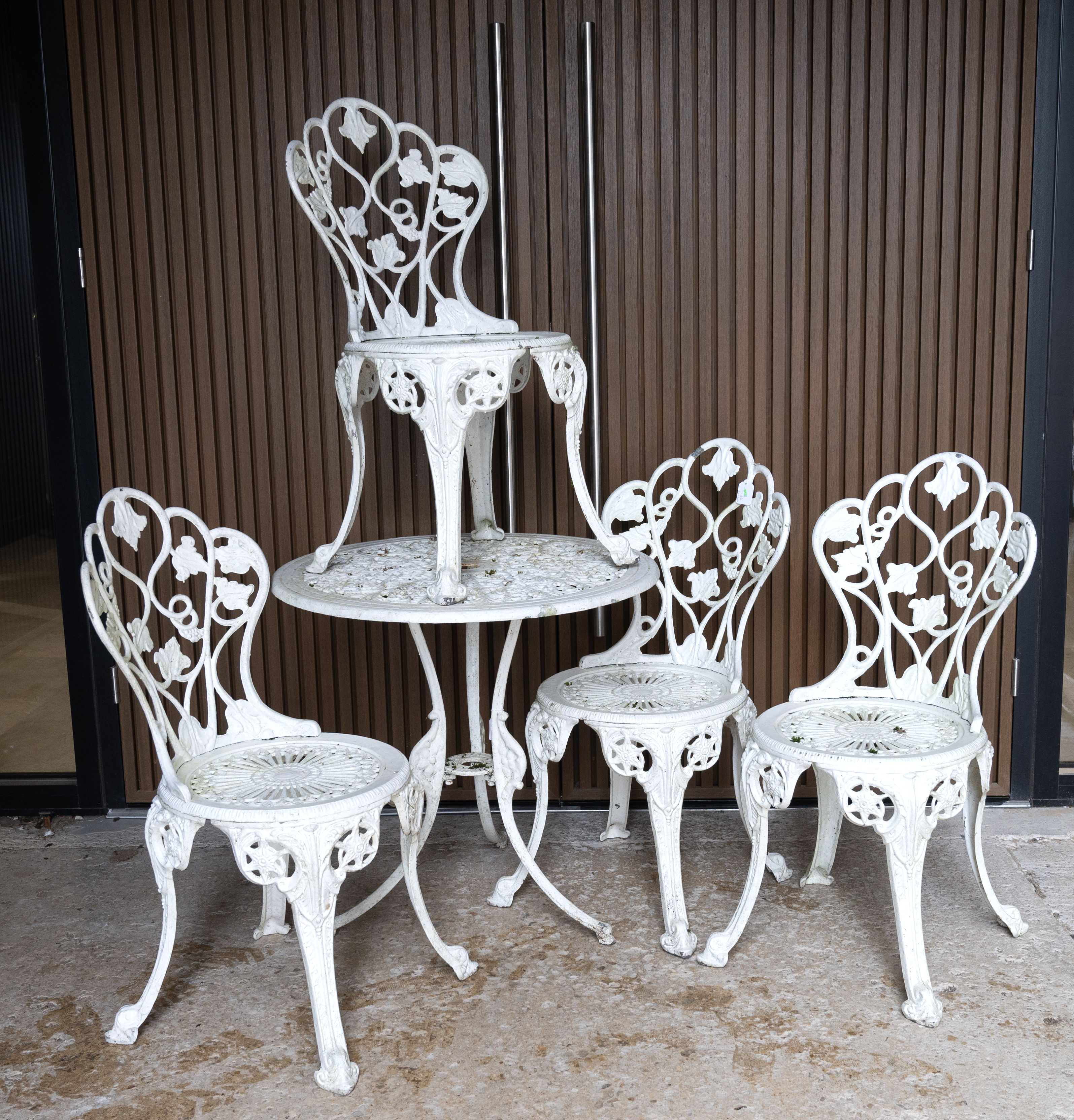 Painted metal garden circular table and four chairs. Vine leaf decoration to backs of chairs. Tab...