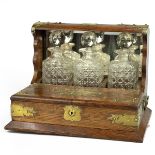 Edwardian brass bound oak Tantalus with three cut glass hobnail decanters and hinged covers openi...
